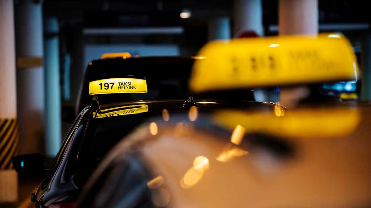 Illuminated yellow Taksi Helsinki roof signs on two dark taxis waiting in a covered rank
