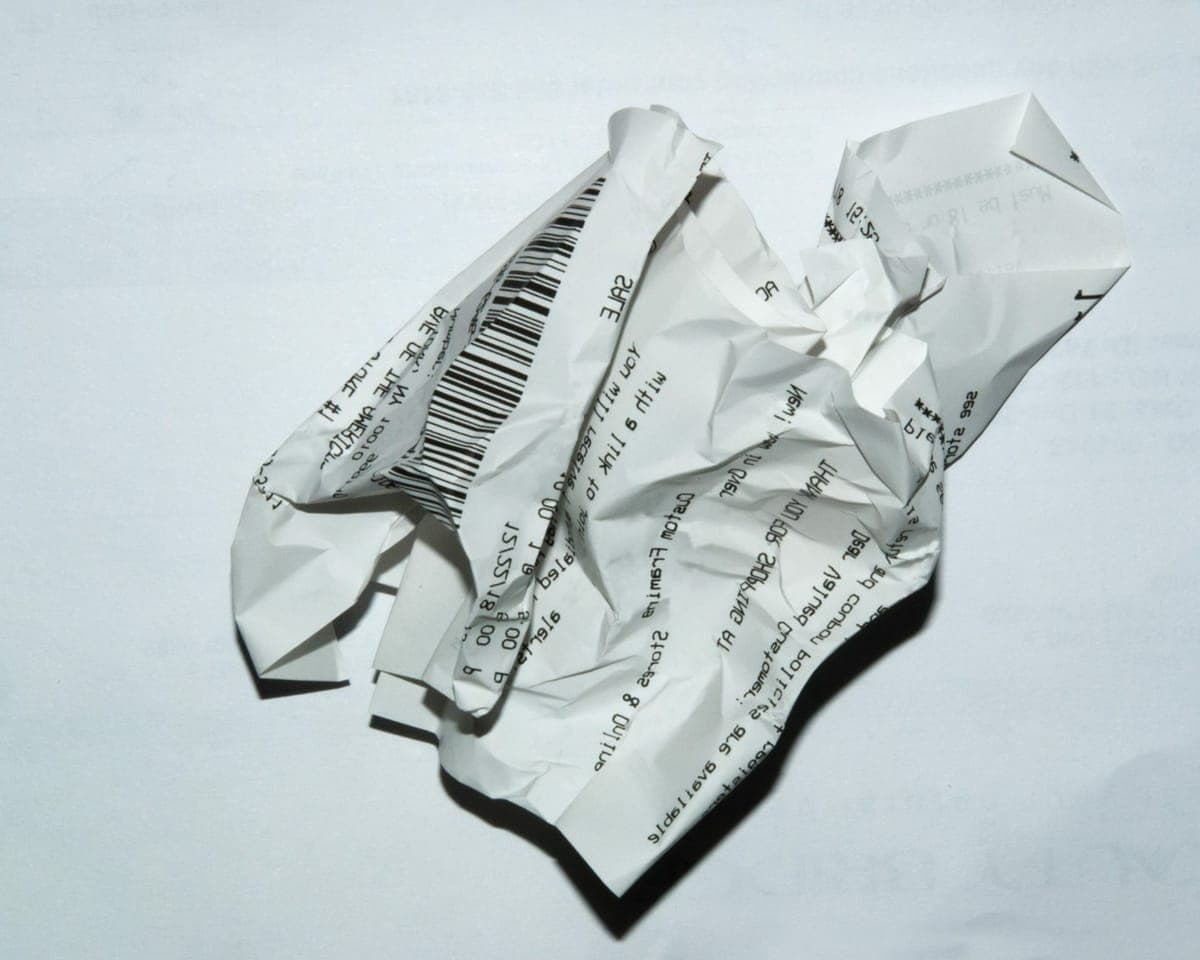 A crumpled paper till receipt lying on a white surface, its barcode and printed text still legible