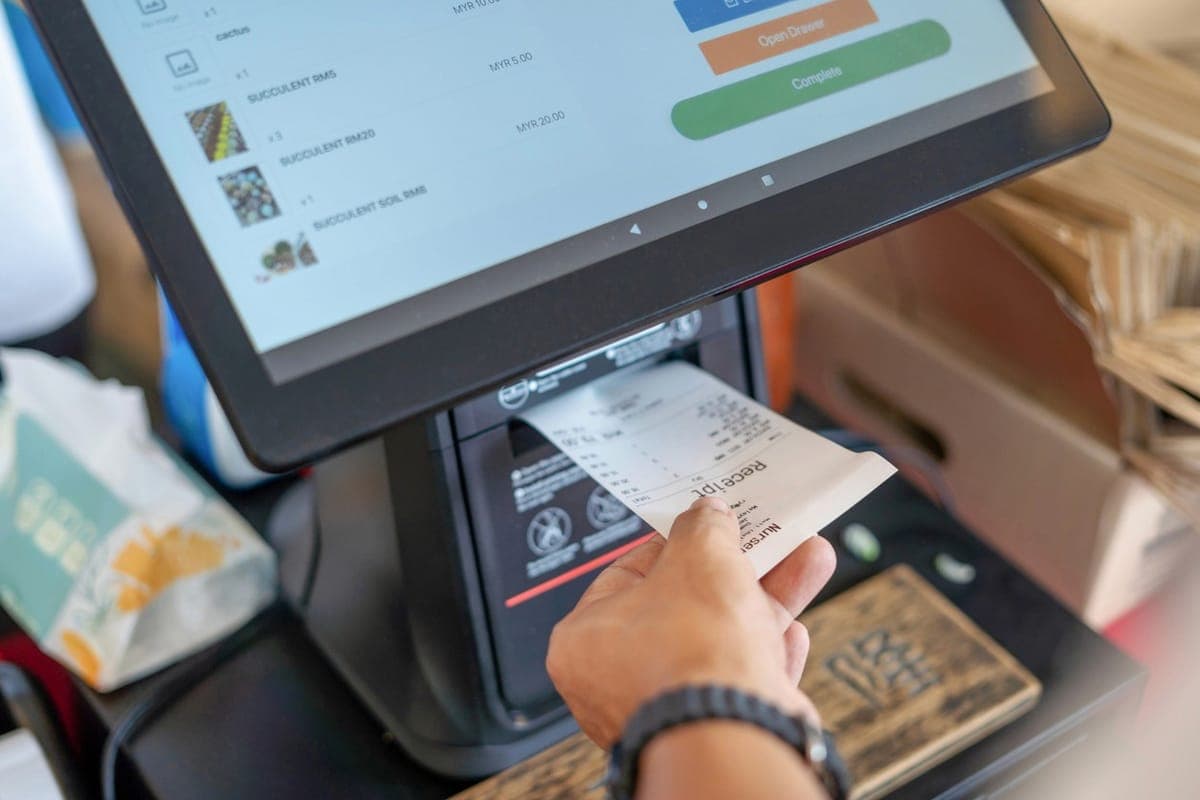 A customer taking a printed receipt from a countertop POS terminal as the order total shows on screen