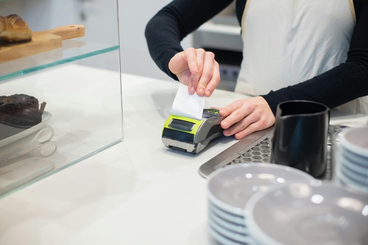A cafe worker tearing a printed paper receipt from a card terminal at the counter