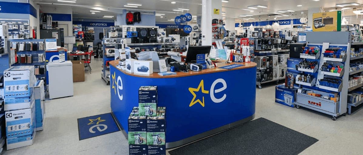 The interior of a Euronics electronics store, with a blue service counter in the centre and appliances on the shelves around it