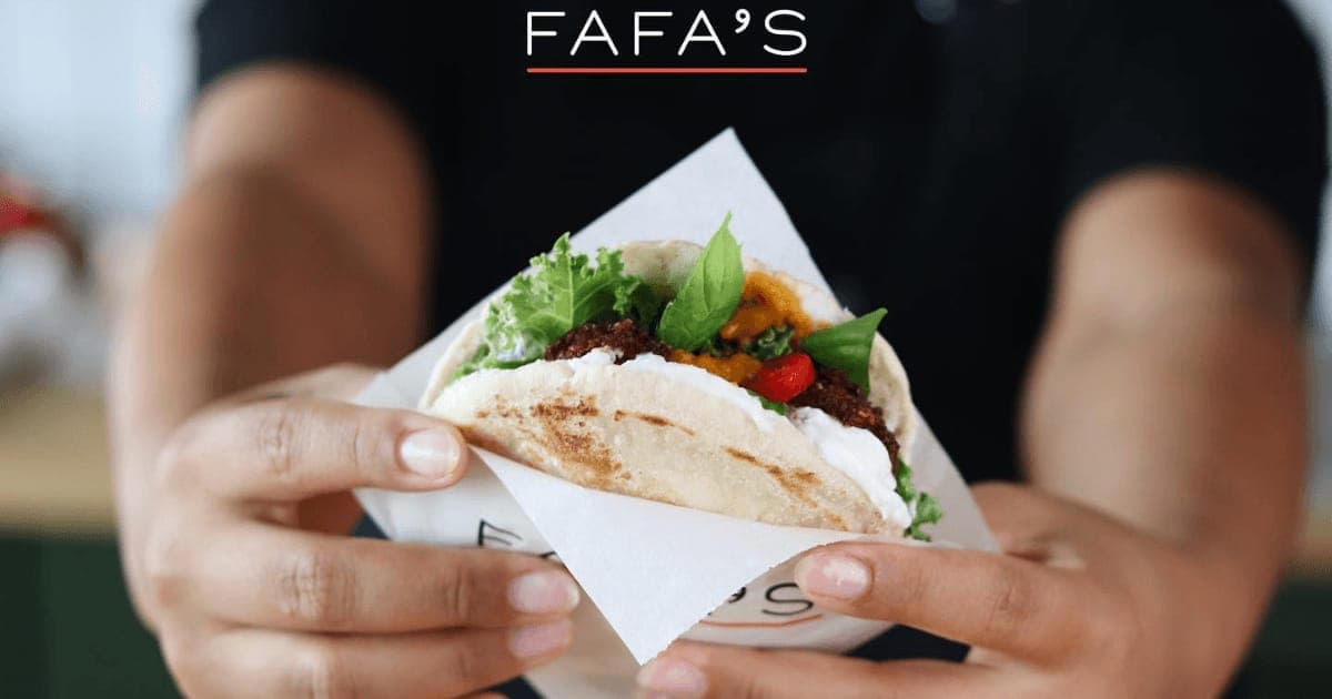 Hands holding a filled pita wrapped in paper under the Fafa's logo