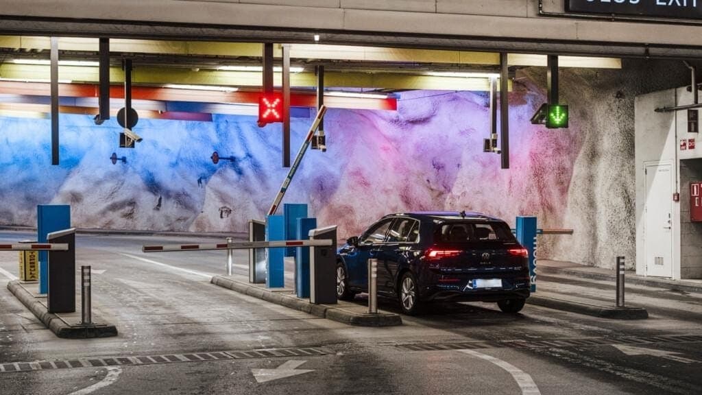 A dark hatchback at the barrier of an underground car park, the exit arrow lit green