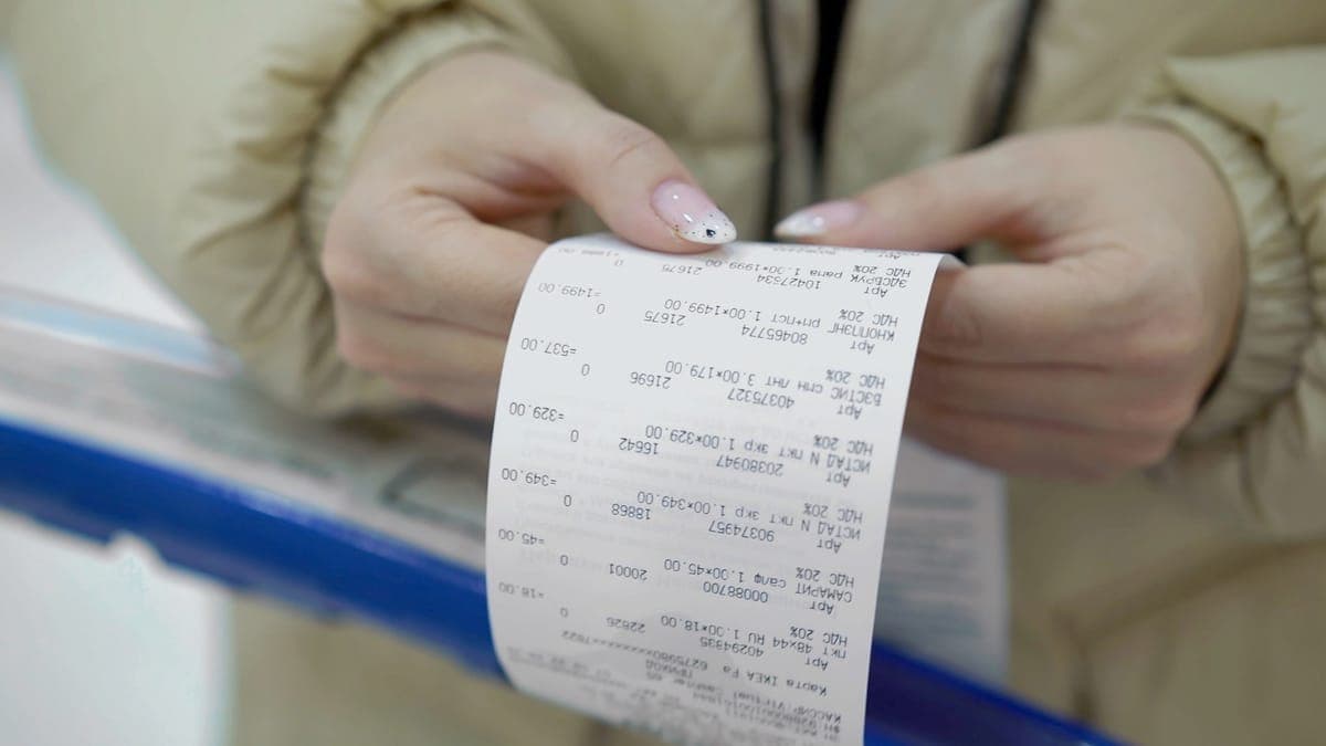 Hands unrolling a long paper till receipt printed with itemised lines and VAT