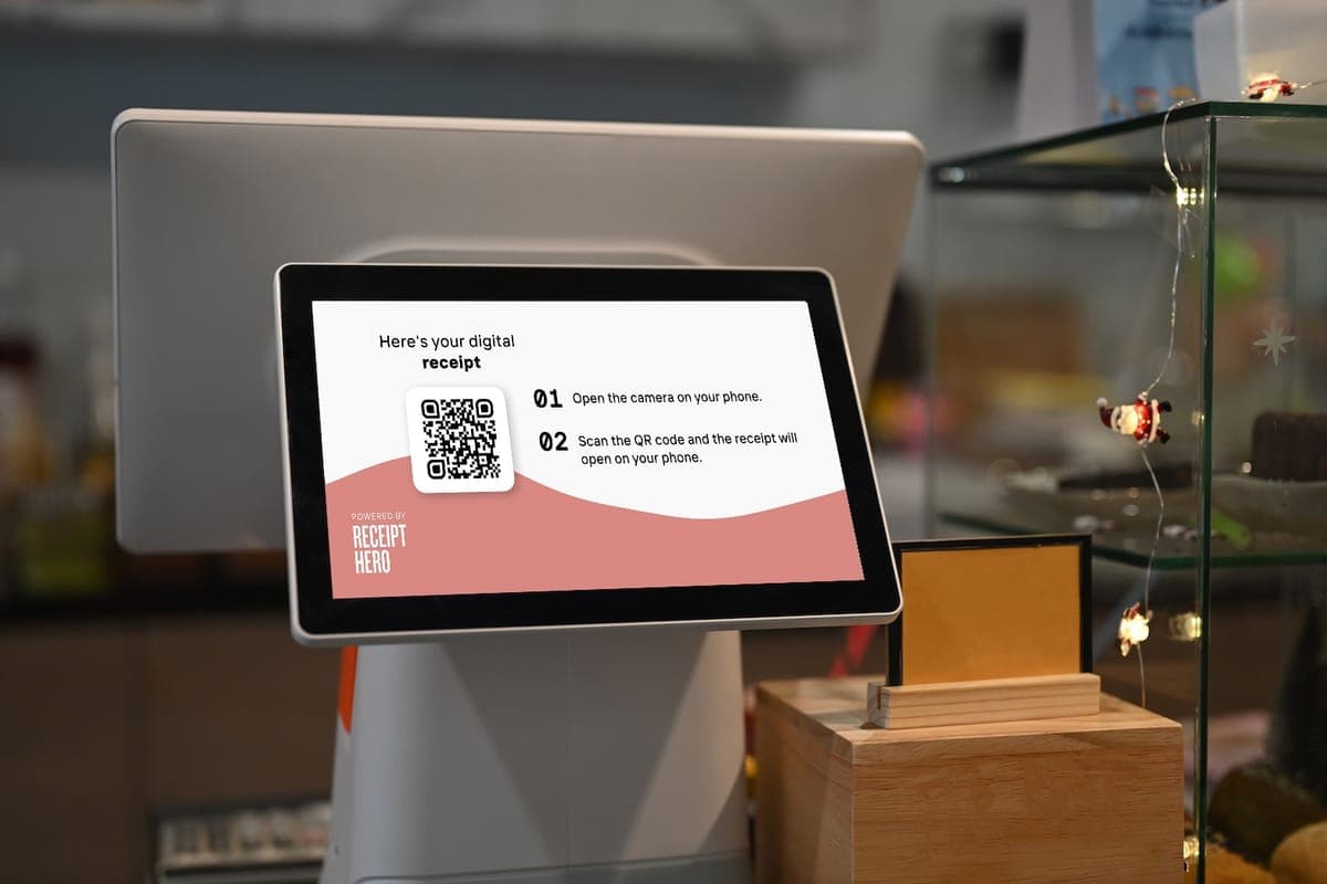 A countertop till screen showing a QR code with two steps: open the camera on your phone, scan the code and the receipt opens