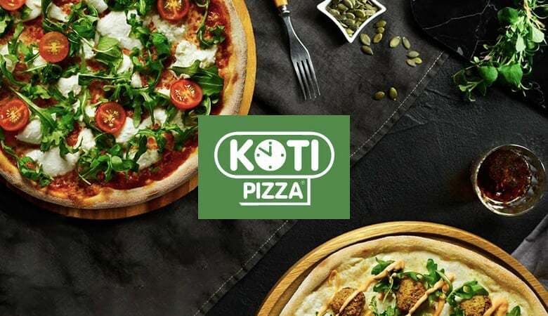 Two Kotipizza pizzas photographed from above on a dark slate table, with the Kotipizza logo between them
