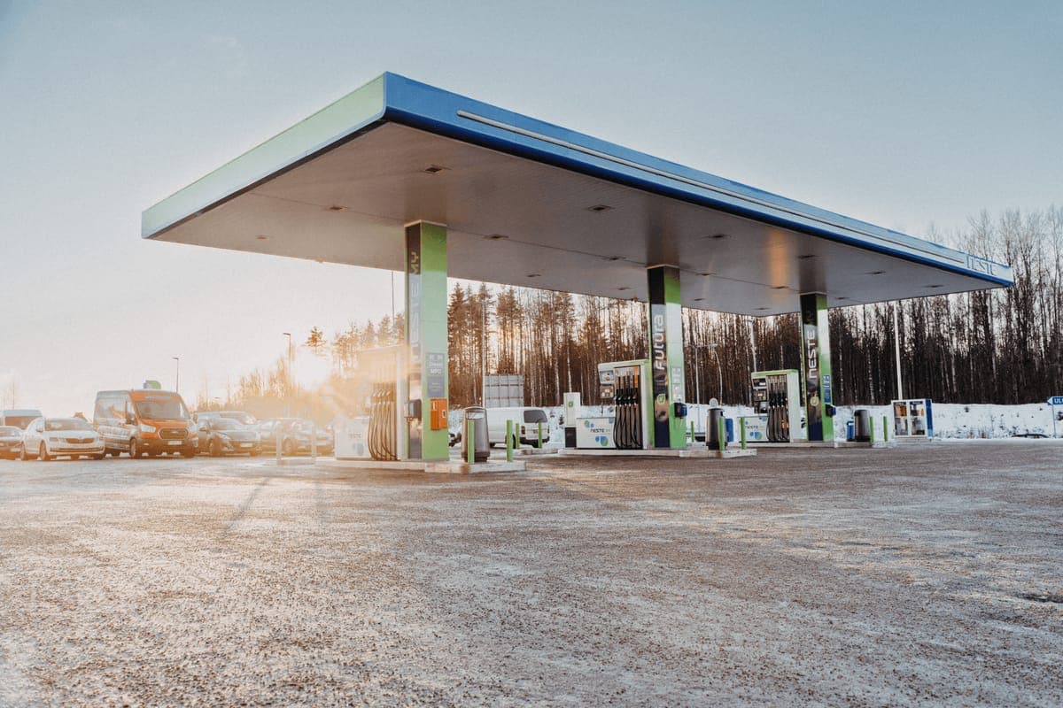 A Neste forecourt in winter at low sun, its canopy over the pumps and a treeline behind
