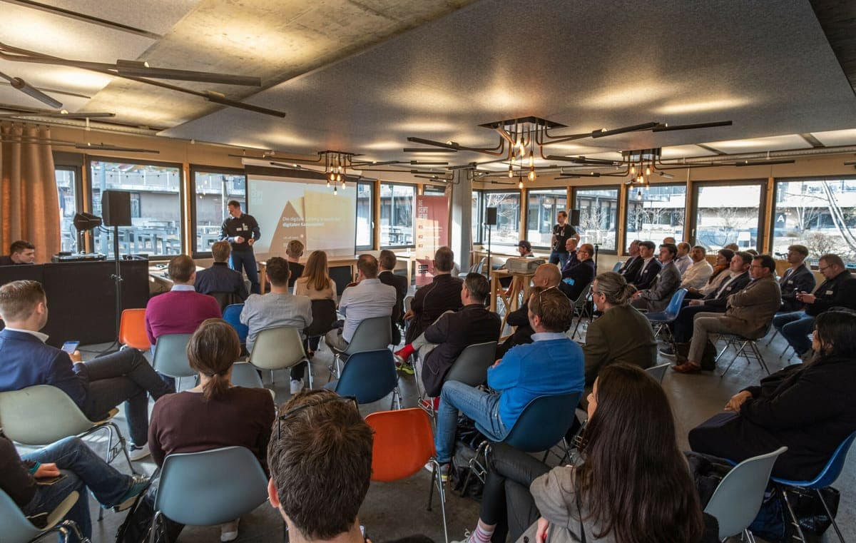 A seated audience at an afterwork event in Zurich watching a speaker present beside a projector screen