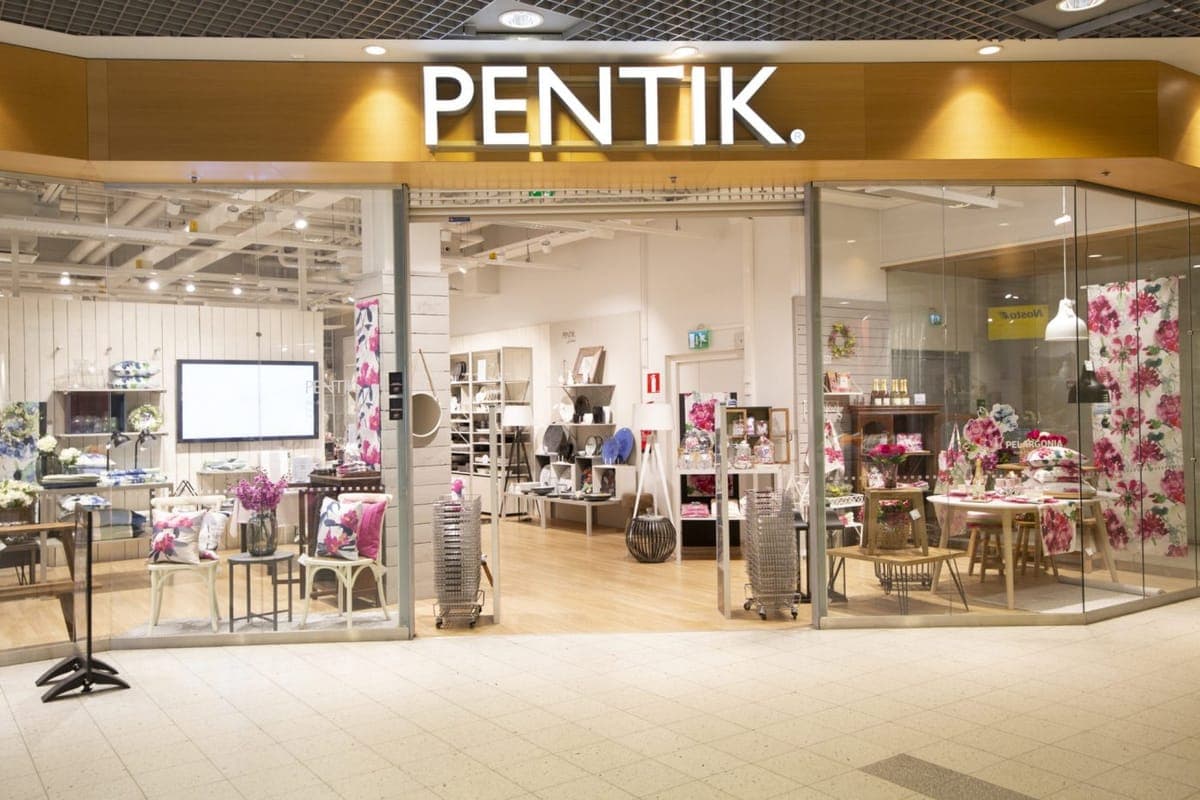 The lit shopfront of a Pentik homeware store in a shopping centre, with floral textiles and tableware displayed inside