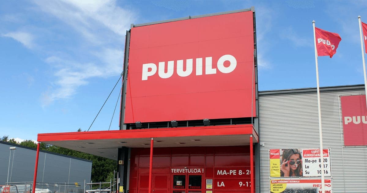The exterior of a Puuilo store on a sunny day, its red sign above the entrance and branded flags flying
