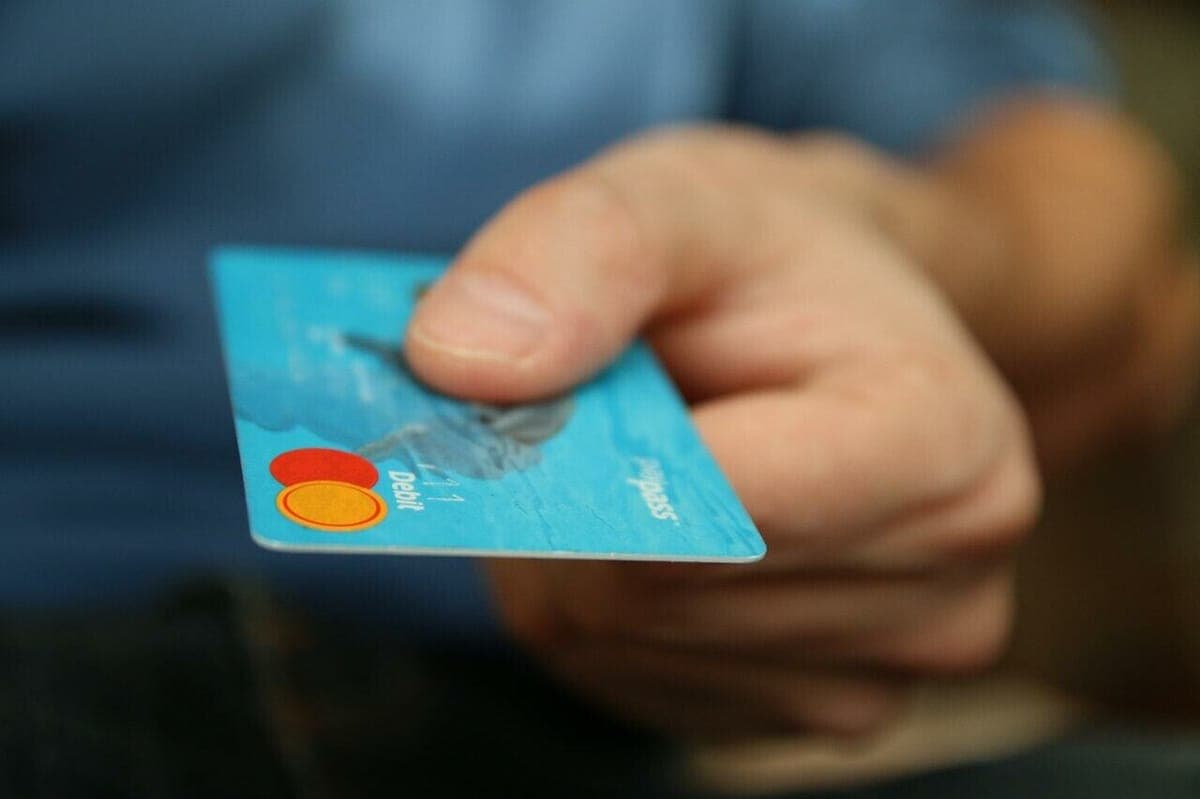 A hand holding out a blue contactless Mastercard debit card