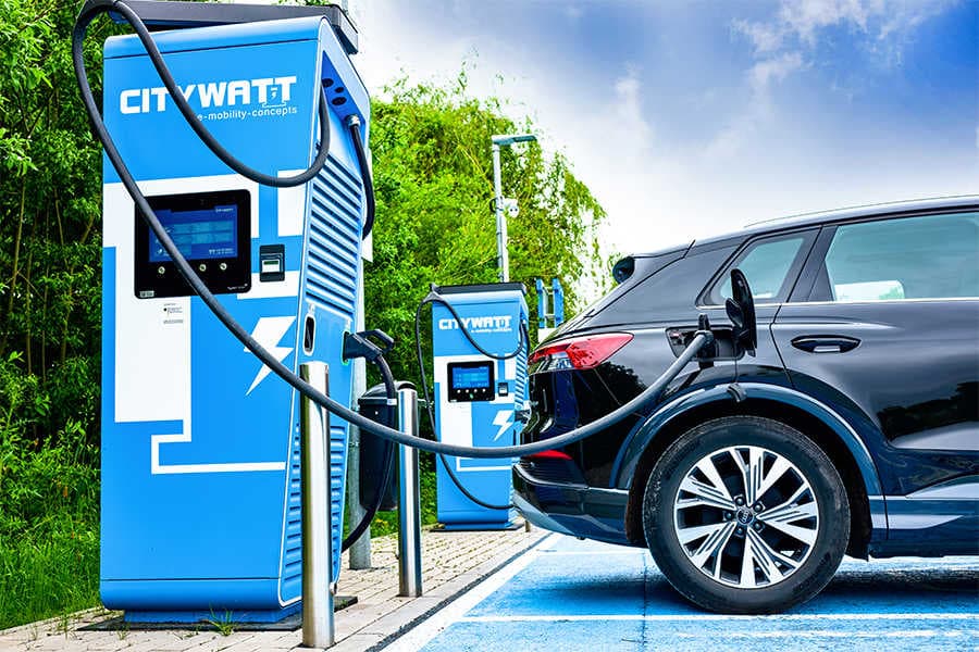 A black electric SUV plugged into a blue Citywatt fast charger at an outdoor charging bay