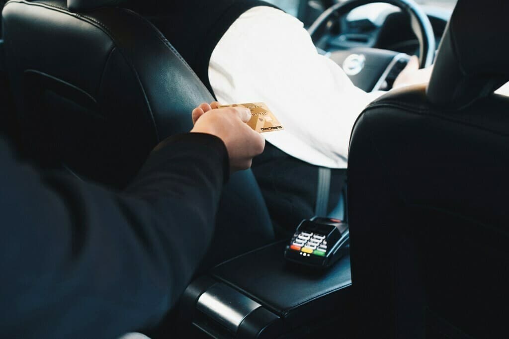 A passenger in the back of a car handing a gold Eurocard forward, a card terminal on the console