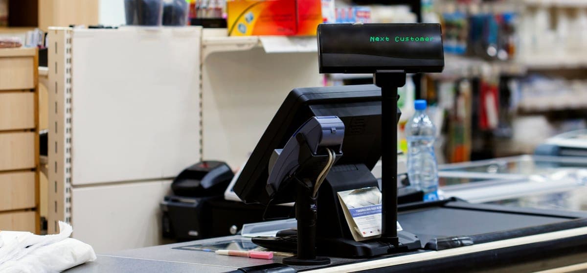 A supermarket checkout with a customer display reading Next Customer above the till