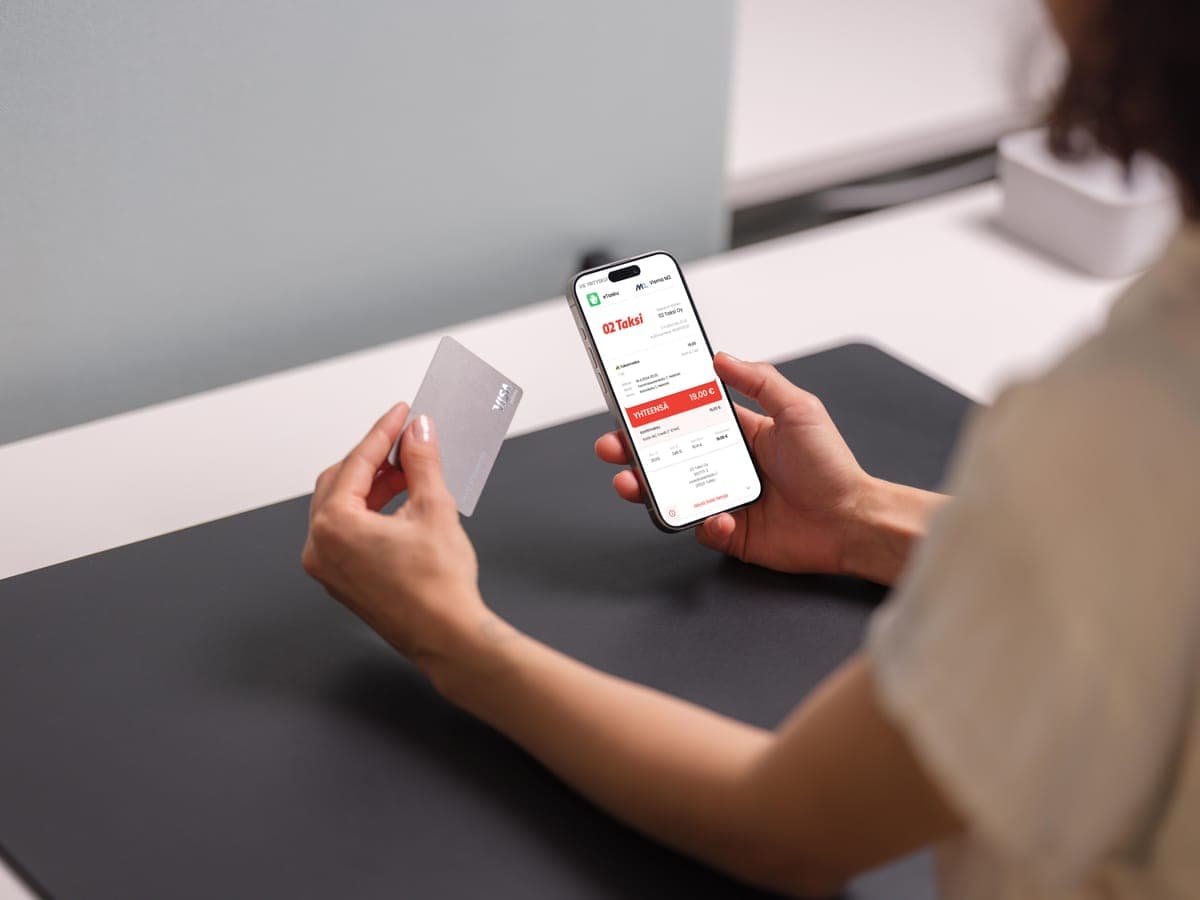 A person holding a Visa card and a phone showing an 02 Taksi digital receipt totalling 18 euros