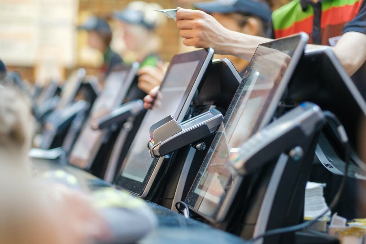 A row of tills at a busy counter, a member of staff reaching across to take a card