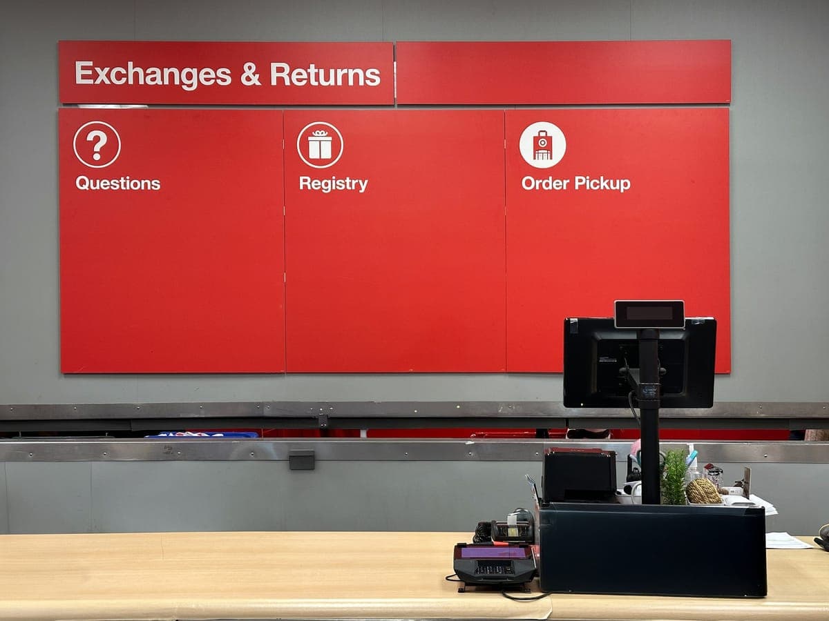 An empty Exchanges and Returns desk in a store, the red sign above it also marking questions, registry and order pickup