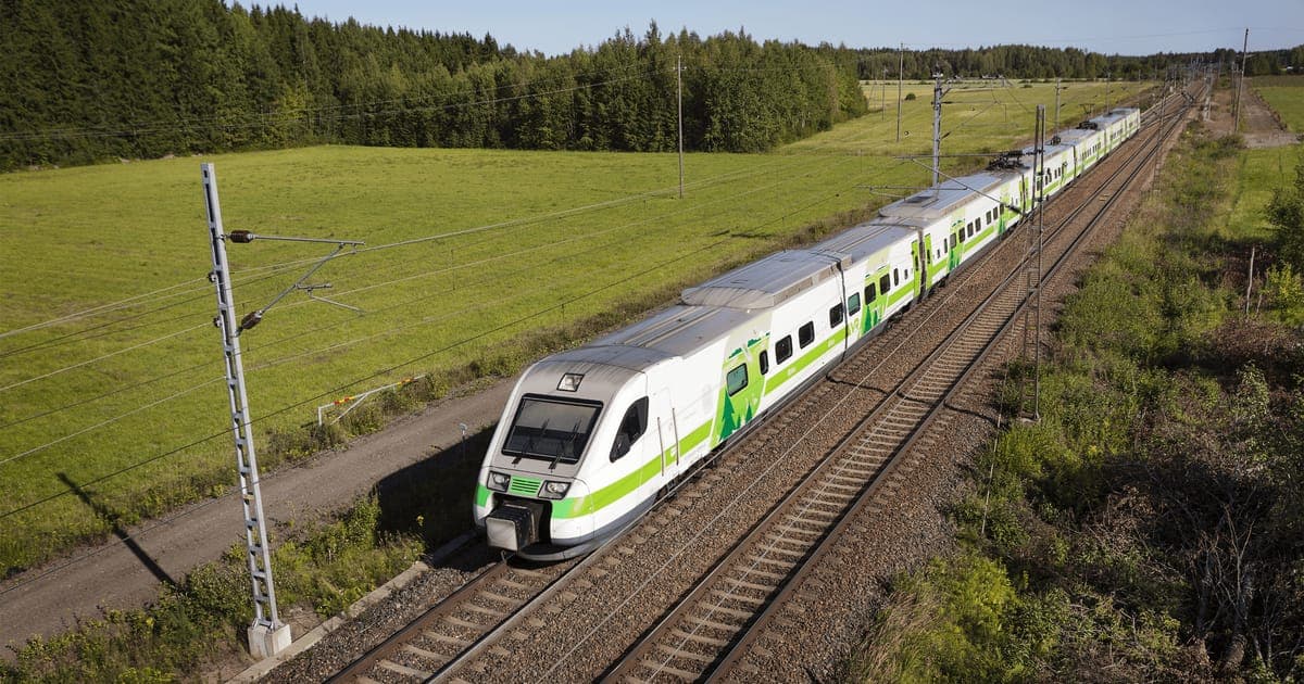 A green and white VR intercity train on the line through Finnish countryside in summer