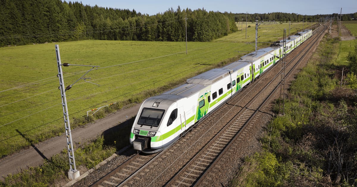 A green and white VR intercity train on the line through Finnish countryside in summer