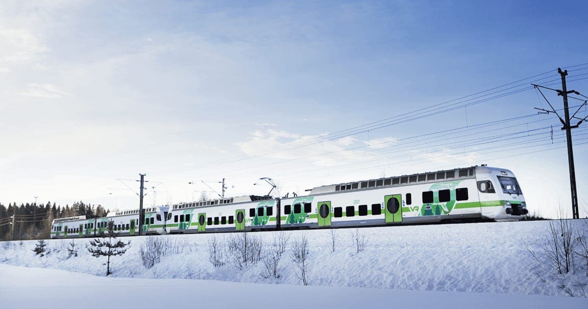 A green and white VR double-decker train crossing a snowy landscape under a pale sky