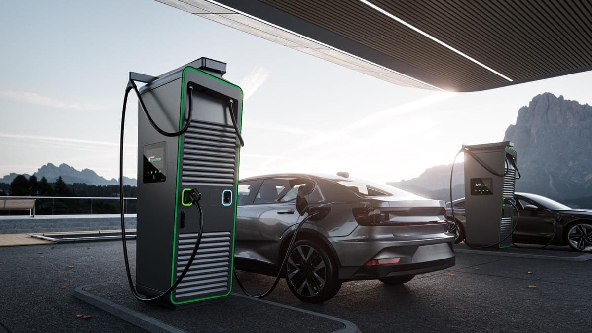 Two cars charging at green-lit fast chargers under a canopy, mountains behind at dusk