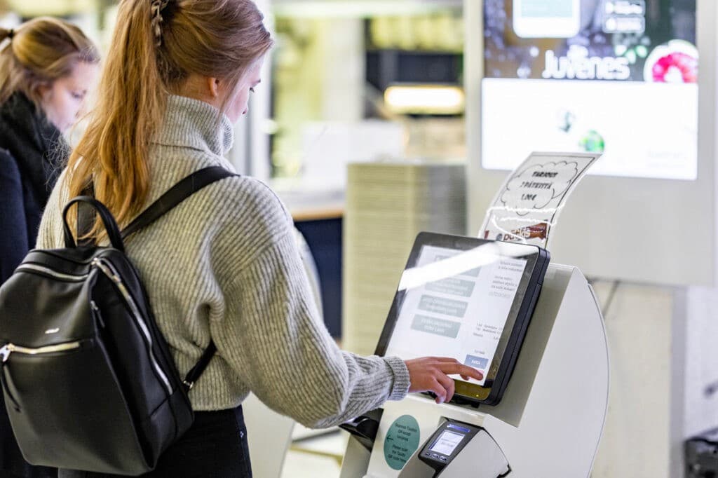 A student with a backpack ordering at a self-service kiosk in a Juvenes cafeteria